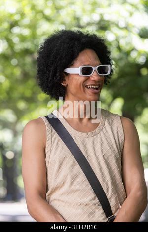 Adulto afro-americano in piedi nel parco sorridente guardando a destra con borsone beige top Shades Foto Stock