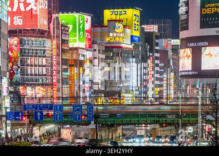 Famoso punto panoramico di Shinjuku. Vista prospettica compressa del ponte ferroviario e del treno sfocato su strade trafficate con molti edifici alle spalle. Notte. Foto Stock