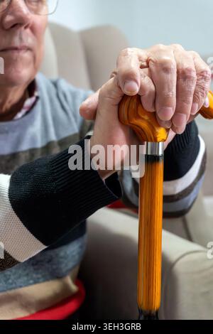 Uomo anziano che tiene il bastone da passeggio in legno che riposa le mani Foto Stock