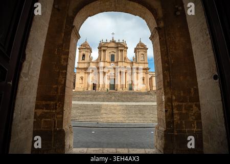 Uno scatto architettonico incorniciato della Cattedrale di San Nicolò in Sicilia, Italia, visto attraverso la monumentale arcata in pietra di Palazzo Du Foto Stock