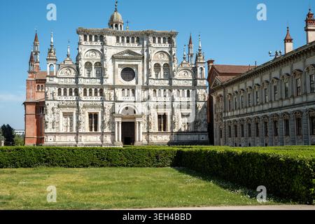 La facciata in marmo ornata della Certosa di Pavia si erge ben dietro una curata siepe e prato verde. Questo capolavoro Foto Stock