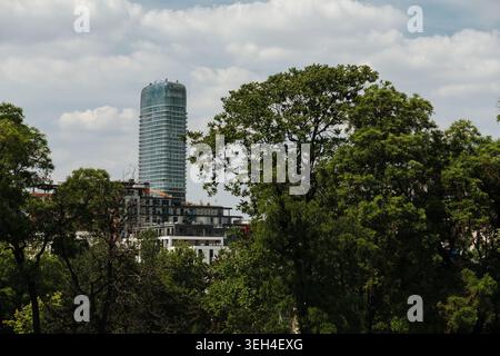 Un moderno grattacielo di vetro si erge dietro alberi verdi a Belgrado, Serbia. Concetto di crescita urbana sostenibile, business e natura urbana. Foto Stock