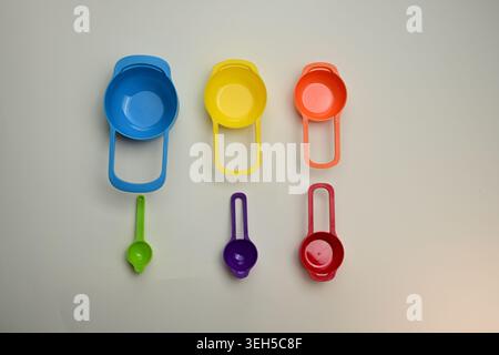 Tazze e cucchiai da misurazione in plastica colorati disposti in un flat lay, strumenti da cucina luminosi per cucinare, infornare e porzioni precise di ingredienti. Foto Stock