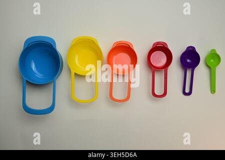 Tazze e cucchiai da misurazione in plastica colorati disposti in un flat lay, strumenti da cucina luminosi per cucinare, infornare e porzioni precise di ingredienti. Foto Stock