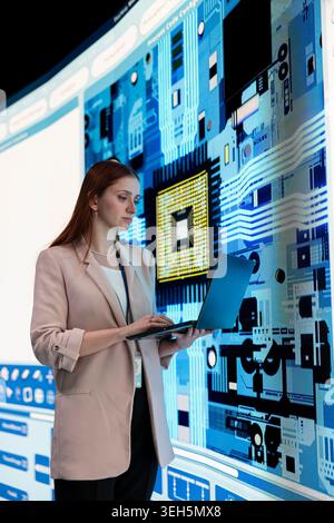 Donna in un impianto di produzione di microchip che utilizza un computer portatile per aggiornare il circuito elettronico su display digitale. Ingegnere donna che guarda i semiconduttori in silicio sullo schermo, facendo ricerche sulla produzione Foto Stock