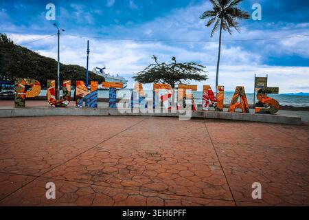 Puntarenas, Costa Rica - 19 ottobre 2025: Vivace cartello a mosaico sulla passerella del Paseo de los Turistas con una nave da crociera ancorata al Foto Stock