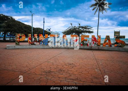 Puntarenas, Costa Rica - 19 ottobre 2025: Vivace cartello a mosaico sulla passerella del Paseo de los Turistas con una nave da crociera ancorata al Foto Stock