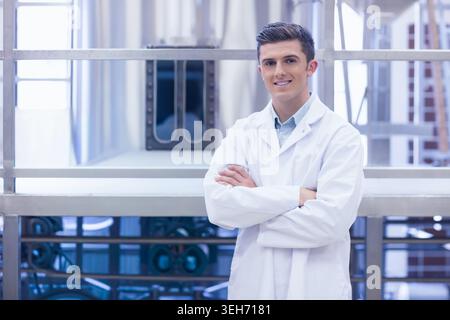 Uomo negli anni '20 in piedi che indossa le braccia incrociate bianche di fronte alla telecamera negli impianti industriali Foto Stock