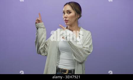 Donna punta il dito indice verso l'alto e gesti con l'altra mano in studio con sfondo viola; curiosità scoperta. Foto Stock