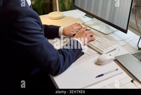 Uomo d'affari che digita i dati finanziari sulla tastiera durante l'audit contabile in ufficio Foto Stock