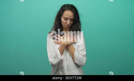 Donna che preme le mani sul petto con gli occhi chiusi in uno sfondo di studio color verde acqua, mostrando un gesto espressivo e sincero di sincerità e sollievo; premuroso Foto Stock