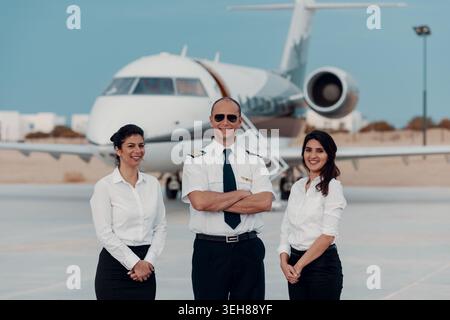 Il pilota e due membri dell'equipaggio posano di fronte al jet privato sull'asfalto dell'aeroporto per i viaggi di lavoro Foto Stock