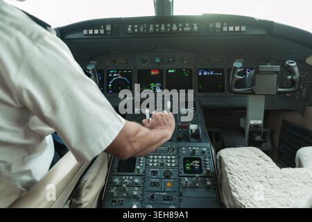 Pilota che controlla i comandi in una cabina di pilotaggio privata con strumenti illuminati e vista della cabina di pilotaggio Foto Stock