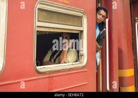 Sri Lanka - 06 febbraio 2026: Vista dei passeggeri su un treno rosso con una donna che guarda fuori dalla finestra e un uomo che si appoggia dalla porta. Foto Stock