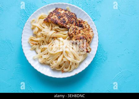 Primo piano di tagliatelle salate con pollo fritto croccante servito su un vivace sfondo blu Foto Stock