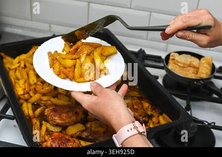 La spatola da cucina mette una grande porzione di patate sul piatto bianco. La spatola da cucina serve piatti arrostiti fatti in casa per cena. Patate dorate con spicchi di patate Foto Stock