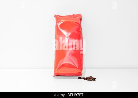 Sacchetto ermetico rosso brillante con chicchi di caffè su una superficie bianca. Foto Stock