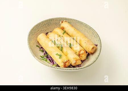 Un primo piano di quattro rotoli di carta di riso tagliati a metà diagonalmente, rivelando gli strati geometrici di lattuga, menta, spaghetti di riso e gamberi, su un legno chiaro Foto Stock
