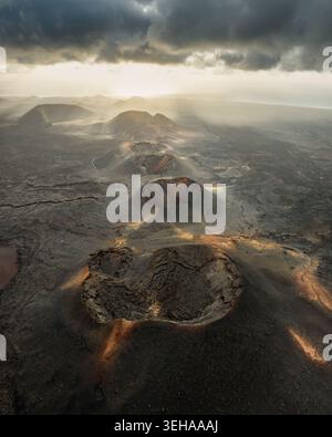 Vista aerea dei crateri vulcanici del Parco Nazionale di Timanfaya e dei vasti campi di lava sotto un cielo spettacolare con raggi del sole a Lanzarote, Canarias, Spagna. Foto Stock