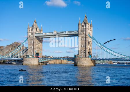 Il Tower Bridge si erge maestosamente sul Tamigi, mostrando il suo design iconico. Una piccola barca scivola mentre un uccello vola nel cielo azzurro Foto Stock
