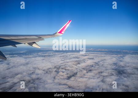 Ala degli aeroplani in volo con livrea blu e cremisi contro il cielo e lo sfondo di terra Foto Stock
