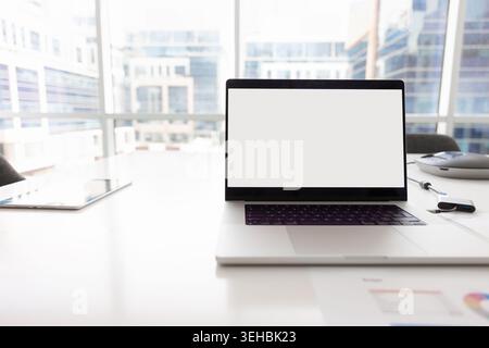 Documenti con grafici accanto al notebook con schermo bianco per il mockup Foto Stock