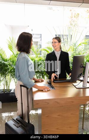 Donna ospite dell'hotel con valigia in piedi alla reception Foto Stock