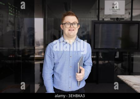 Giovane con la sindrome di Down sorridente, in posa in ufficio Foto Stock