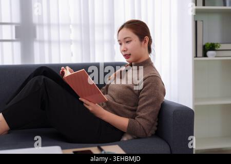 Donna d'affari asiatica che legge un libro sul divano a casa rilassante pianificazione sviluppo professionale apprendimento strategia educazione Foto Stock