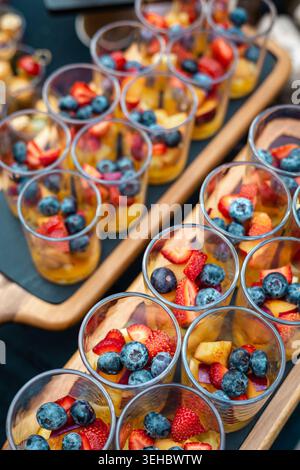 Bicchieri trasparenti a strati di fragole, mirtilli e frutti gialli esposti su tavole di ardesia nere con manici in legno. Perfetto per un servizio salutare Foto Stock