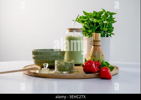 Strumenti Matcha su tavola di legno con polvere sparsa e piccolo vaso di latte accanto alle fragole fresche. Atmosfera da laboratorio che unisce artigianato e Mo Foto Stock