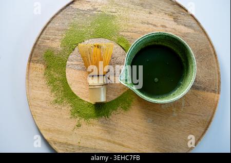 Primo piano di schiuma di matcha verde vivace e schiuma in una ciotola di ceramica su un asse di legno con caraffa nelle vicinanze. Bordo testurizzato ricco e colori brillanti. Matcha Foto Stock