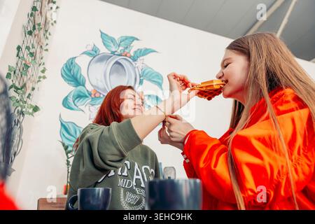 madre e figlia condividono un momento in un bar. La madre ha i capelli rossi e indossa un maglione verde. La figlia ha lunghi capelli castani ed è in una Foto Stock