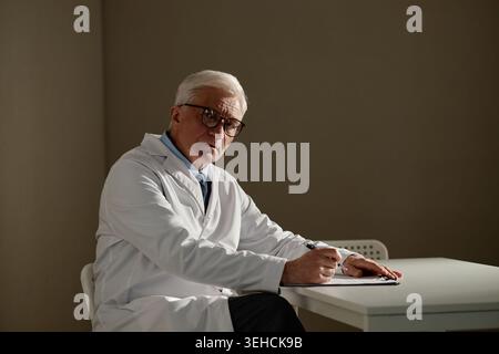 Ritratto del medico maschio anziano che scrive Note di salute mentale Foto Stock