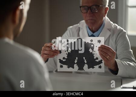 Senior maschio terapista che mostra il test di Inkblot durante la sessione di salute mentale Foto Stock