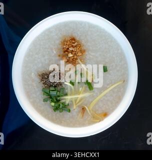 La vista dall'alto del porridge di riso o della zuppa di riso o del riso bollito con spezie e carne di pollo in una ciotola bianca è isolata su sfondo nero. Foto Stock
