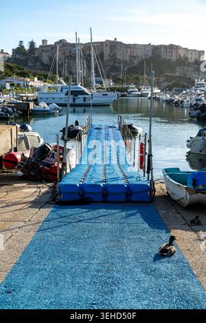 Tropea - Kalabrien - Italia - 05-30-2025: Un molo galleggiante conduce al porto di Tropea, Calabria, con barche ormeggiate su entrambi i lati e edifici storici sullo sfondo. Foto Stock