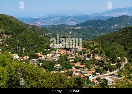 Nydri - Isole Ionie - Grecia - 08-09-2025: Un villaggio di montagna con case sparse e tetti rossi in una valle verde, circondato da colline boscose e catene montuose lontane. Foto Stock
