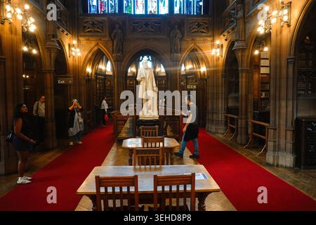 I visitatori della storica Reading Room presentano una statua di John Rylands all'interno della John Rylands Library di Manchester, Inghilterra, Regno Unito Foto Stock