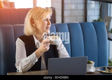 Una donna silenziosa osserva il paesaggio urbano. Una donna anziana in un abbigliamento da lavoro contempla la vista della città in pace. Donna matura in abbigliamento formale Marvels di Urban Foto Stock