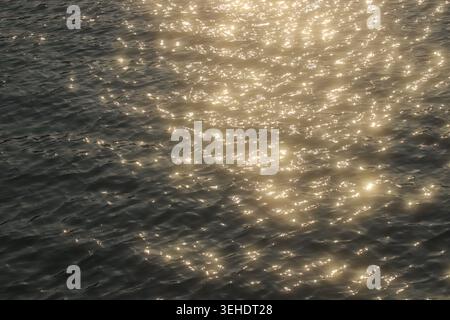 La luce del sole dorata che si riflette sulla superficie ondulata dell'acqua crea motivi astratti scintillanti e una texture elegante e naturale. Foto Stock