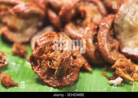 Vista ravvicinata dell'intestino di maiale fritto in pastella croccante e croccante su una foglia di banana verde con pezzi d'aglio fritti, autentico cibo di strada tailandese locale. Foto Stock
