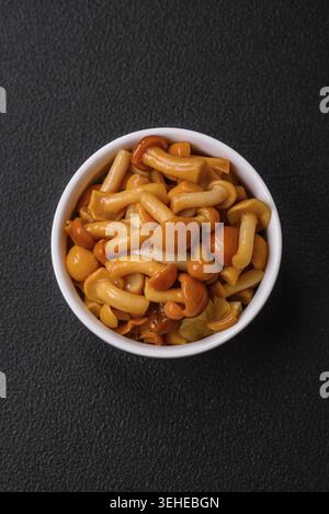 Cibo, deliziosi funghi al miele sottaceto con sale e spezie in un piatto di ceramica su sfondo scuro Foto Stock