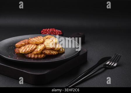 Cibo, deliziose patate fritte croccanti a fette su un piatto di ceramica nera su uno sfondo di cemento scuro Foto Stock