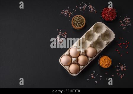 Cibo, uova di pollo crude fresche di colore beige in un vassoio di cartone su sfondo di cemento scuro Foto Stock