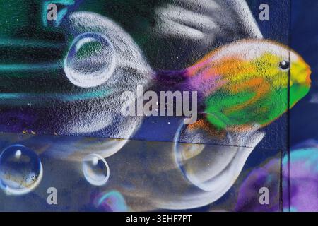 Vivace pesce color arcobaleno che nuota con bollicine trasparenti dettagliato murale di Street art su uno sfondo scuro a Brighton, Inghilterra. Foto Stock