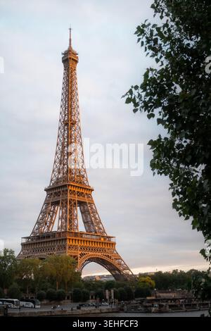 La Torre Eiffel si illumina d'oro alla luce del tramonto serale incorniciata da alberi primaverili lungo la Senna, Champ de Mars, Parigi, Francia, primavera 2026. Foto Stock