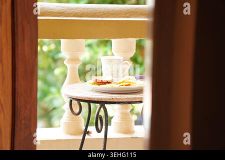 Luminoso balcone per la colazione con tazza di caffè e pasto incorniciato attraverso la porta Foto Stock
