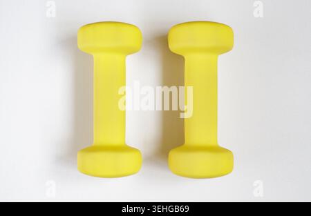 Piccoli manubri gialli su sfondo grigio chiaro, preparati per gli allenamenti domestici. Kettlebell, angolo, fitness, minimalista, soleggiato, pavimento, riutilizzabile. SP Foto Stock