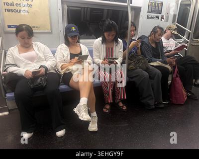 Tutti sono incollati ai loro schermi mentre viaggiano su un treno della metropolitana a New York. Anche se l'uomo dall'altra parte sta leggendo un libro. Foto Stock